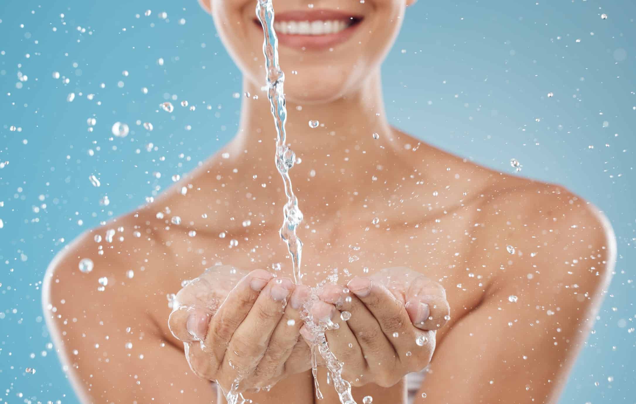 A smiling woman splashes water on her hands, face, and décolleté, enjoying moisturized, intensely hydrated skin from regular HydraFacials.
